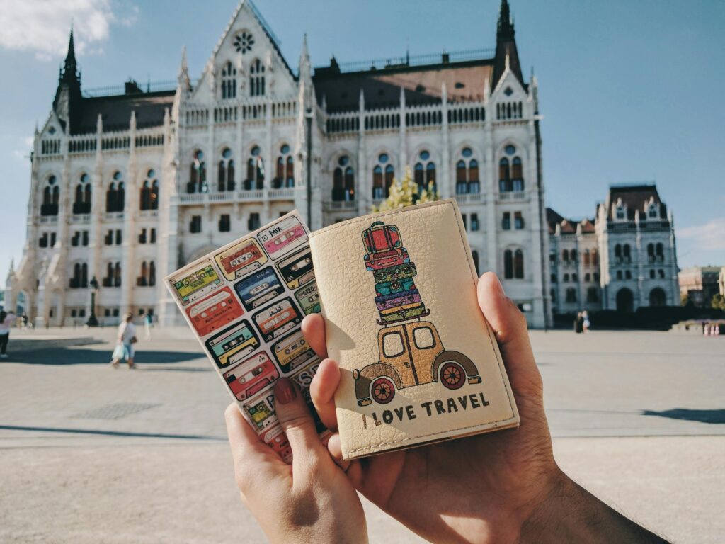 Hands holding travel-themed passports with Budapest Parliament in the background.